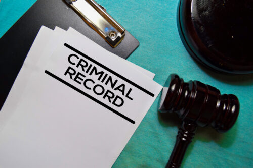 A document labeled "Criminal Record" lies on a clipboard next to a wooden judge’s gavel, symbolizing the gravity of custody decisions, all placed on a blue-green surface.