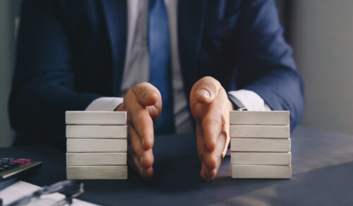 A person in a business suit separates two stacks of wooden blocks on a desk with their hands, symbolizing division or comparison in a professional setting.